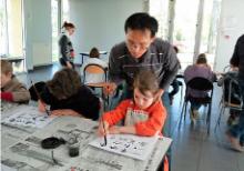 Des enfants pratiquent la caligraphie chinoise sous l'oeil d'un animateur.