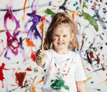 Une petite fille brandissant un pinceau derrière un mur gribouillé