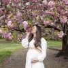 Photo d'une femme enceinte sous un arbre, qui tient son ventre d'une main, et qui sent le parfum des fleurs de l'arbre de l'autre main