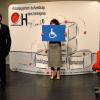 Extrait du spectacle "Embarquez-les !" Une femme tient un panneau avec un pictogramme de personne en fauteuill roulant tandis qu'un homme s'exprime. Tous deux sont devant un paravent "accompagnement du handicap dans l'entreprise".